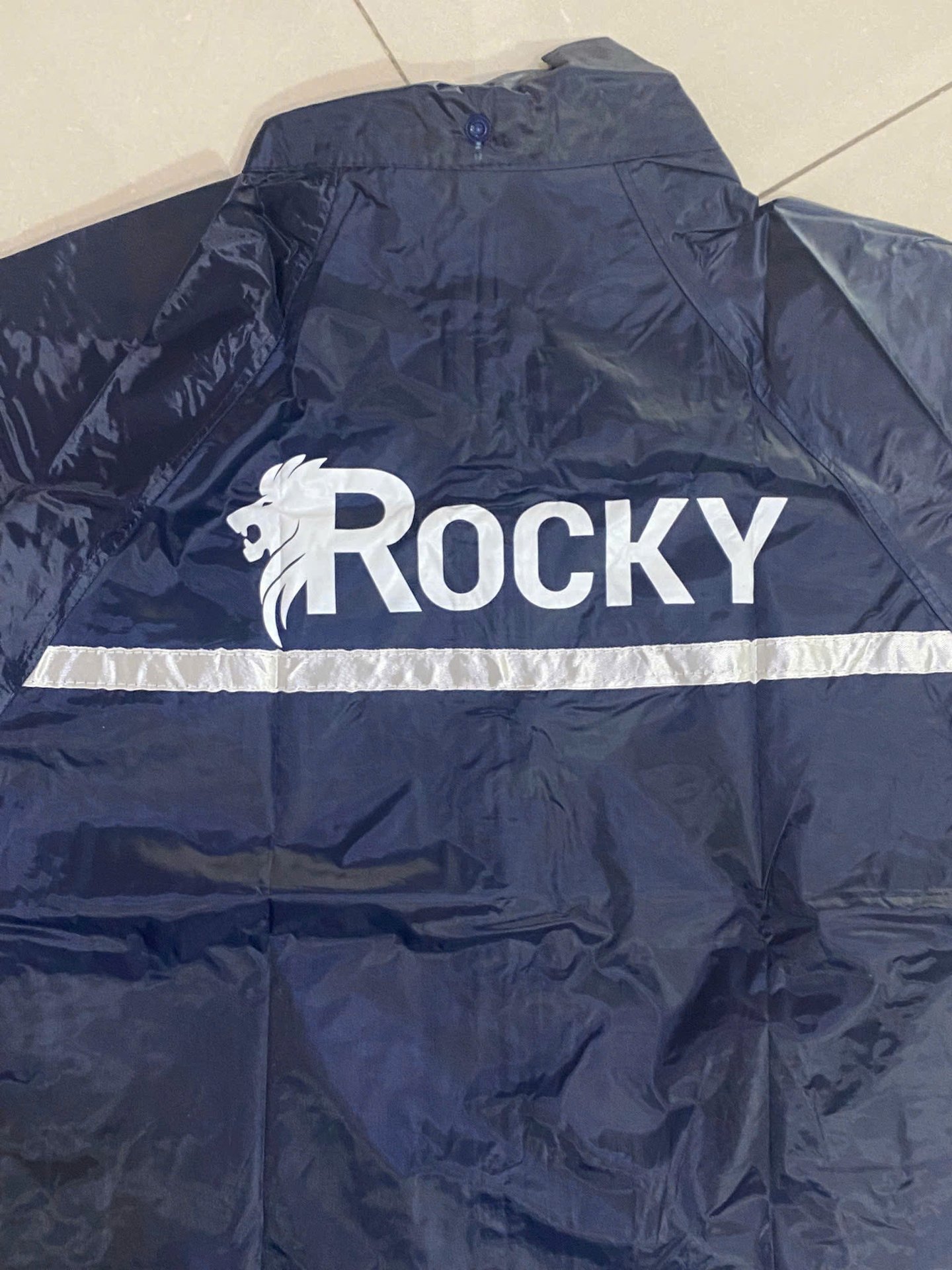 Ảnh cận cổ sau, logo Rocky màu trắng và dải phản quang ngang trên áo mưa xanh đen