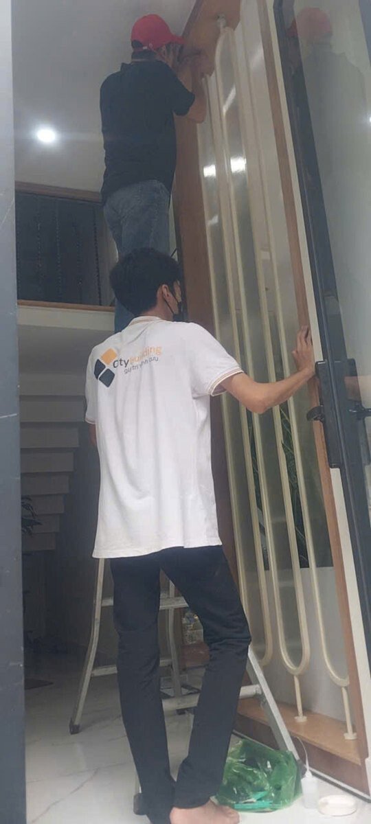 Hai người thao tác với tấm khung bo dài trong nhà