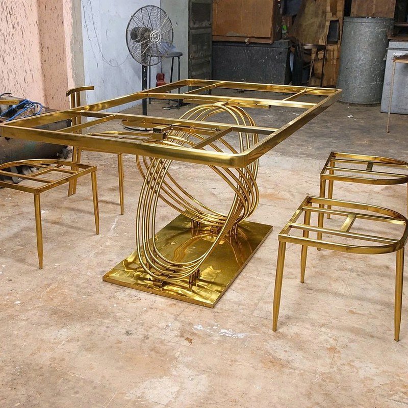 Góc nhìn xiên khung bàn ăn inox PVD với cụm vòng oval giao nhau ở giữa.