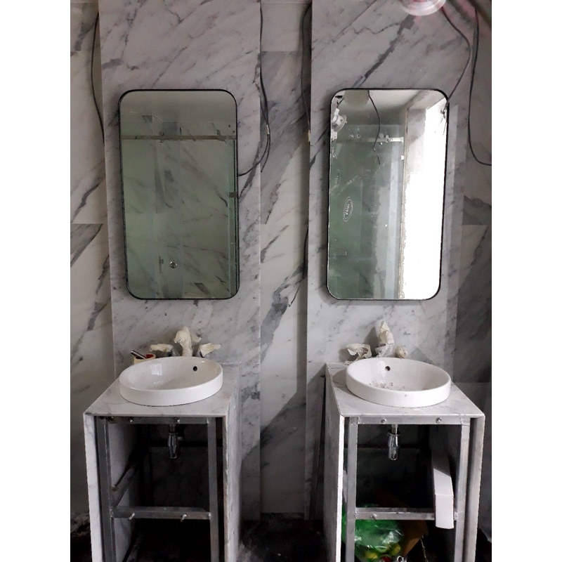 Hai khung lavabo inox đã đặt mặt và chậu tròn, nhìn thấy ống thoát phía dưới; khu vực còn vật tư và lớp bảo vệ.