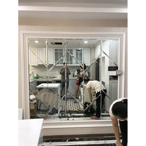 Mảng gương ghép có khung sáng màu phản chiếu người, vật tư và khu vực nội thất đang làm việc.