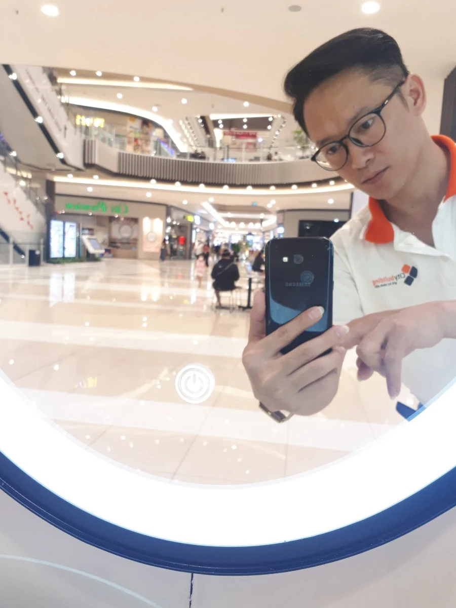 Người đứng trước gương tròn có viền sáng, ngón tay hướng gần biểu tượng tròn trên mặt gương