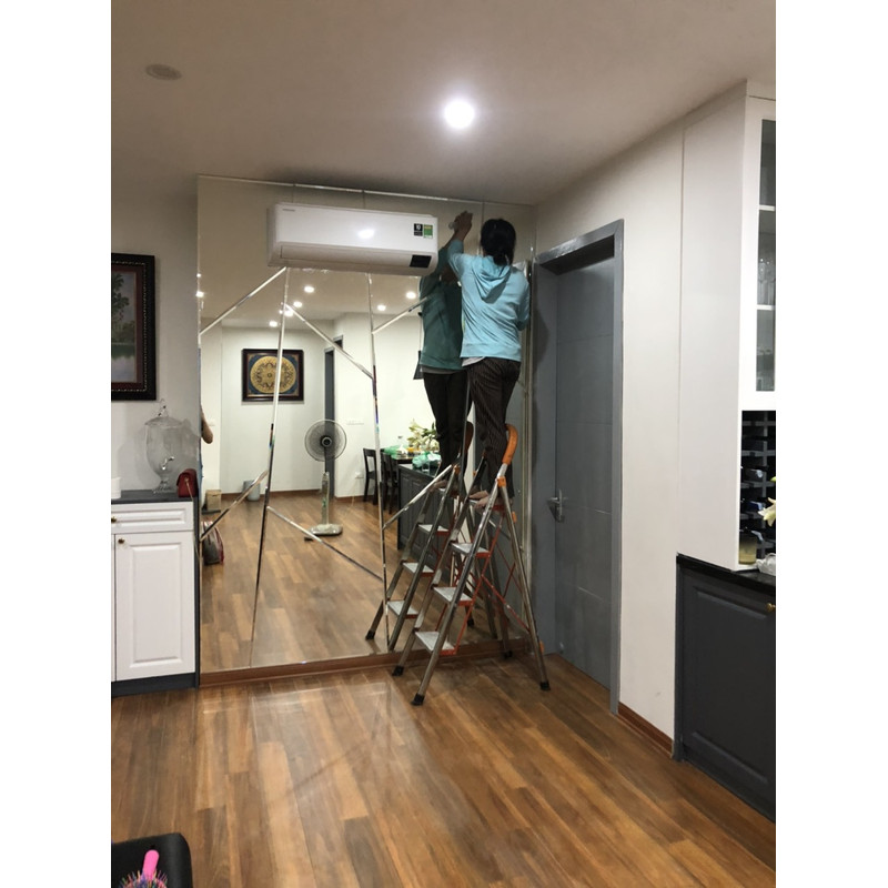 Người đứng trên thang đưa tay tới phần trên của mảng gương ghép, bên dưới có vật tư.