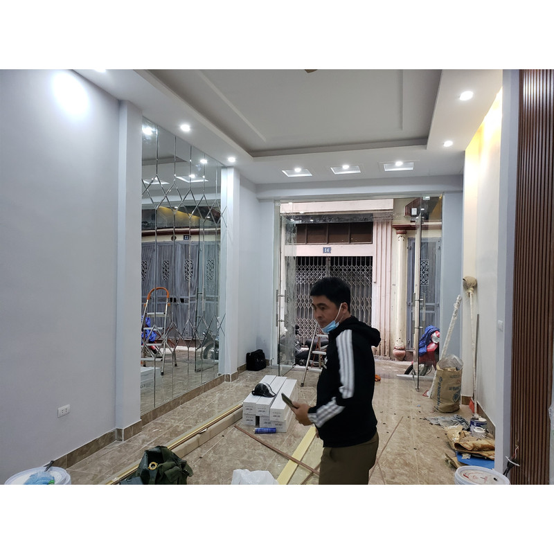 Người trong không gian đang hoàn thiện với mảng gương ghép trên tường, thang và vật tư ở phía dưới.