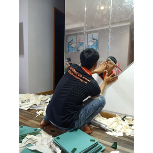 Người ngồi sát sàn, đưa tay tới một tấm gương ở phần dưới của mảng gương ghép.