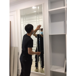 Người đưa tay tới mép mảng gương trong ô tường, bên cạnh hệ kệ màu trắng.