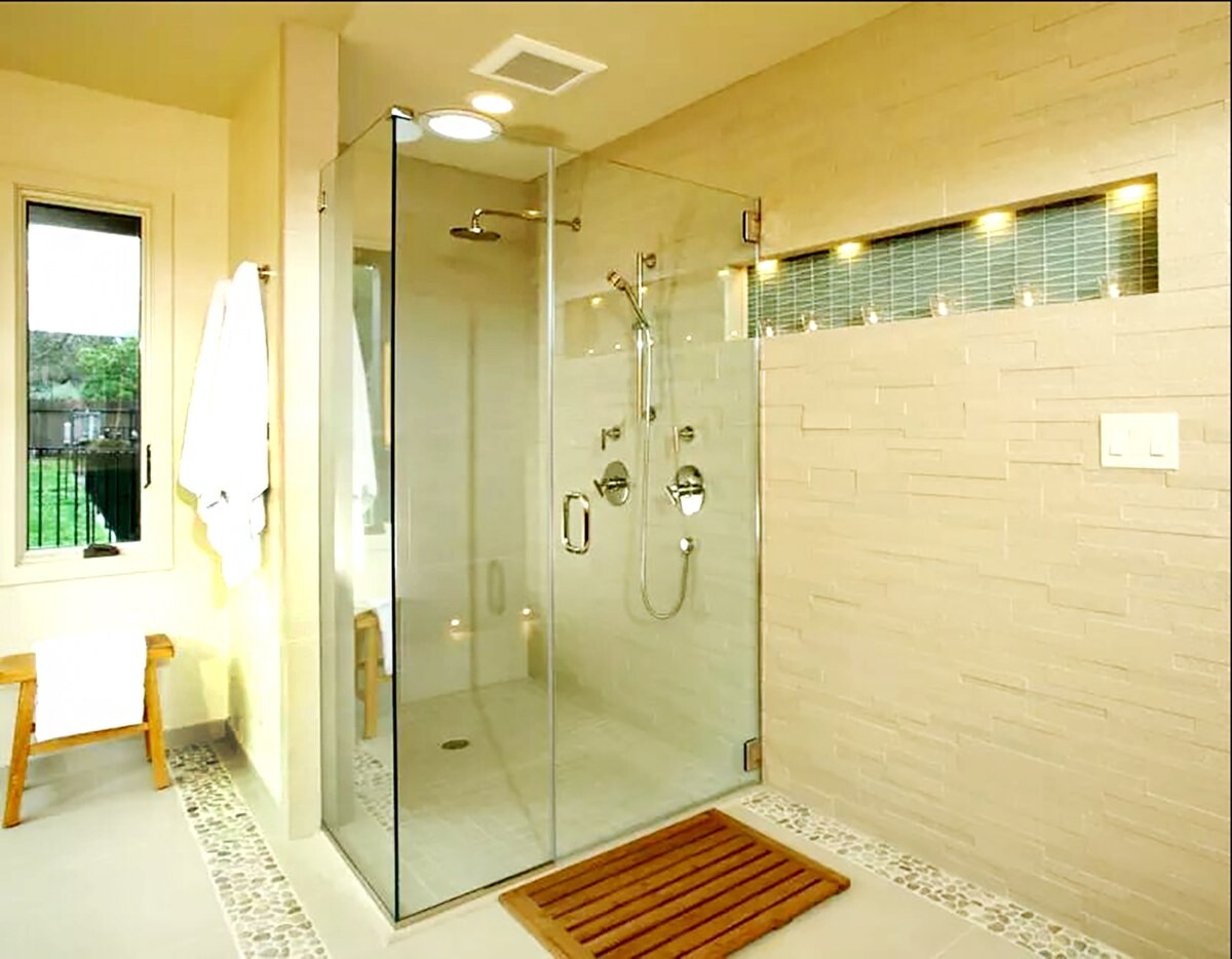 Vách tắm kính góc có cửa mở trong phòng tắm tông vàng sáng