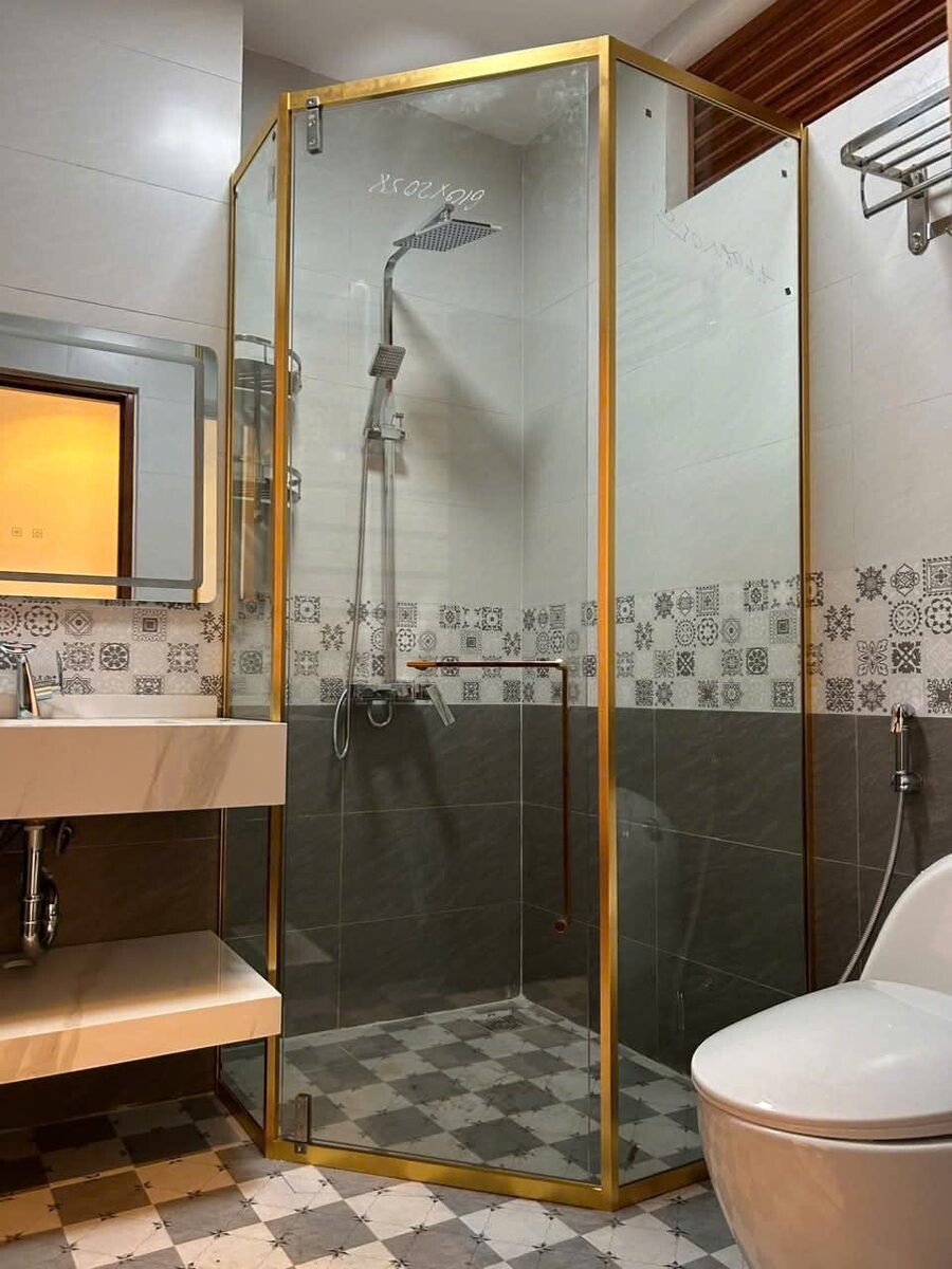 Vách tắm kính viền vàng đặt cạnh chậu rửa trong phòng lát gạch họa tiết