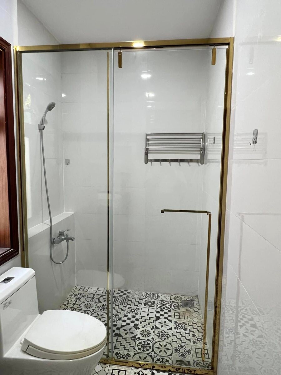 Vách tắm trong suốt có khung và bản lề màu vàng cạnh bồn vệ sinh